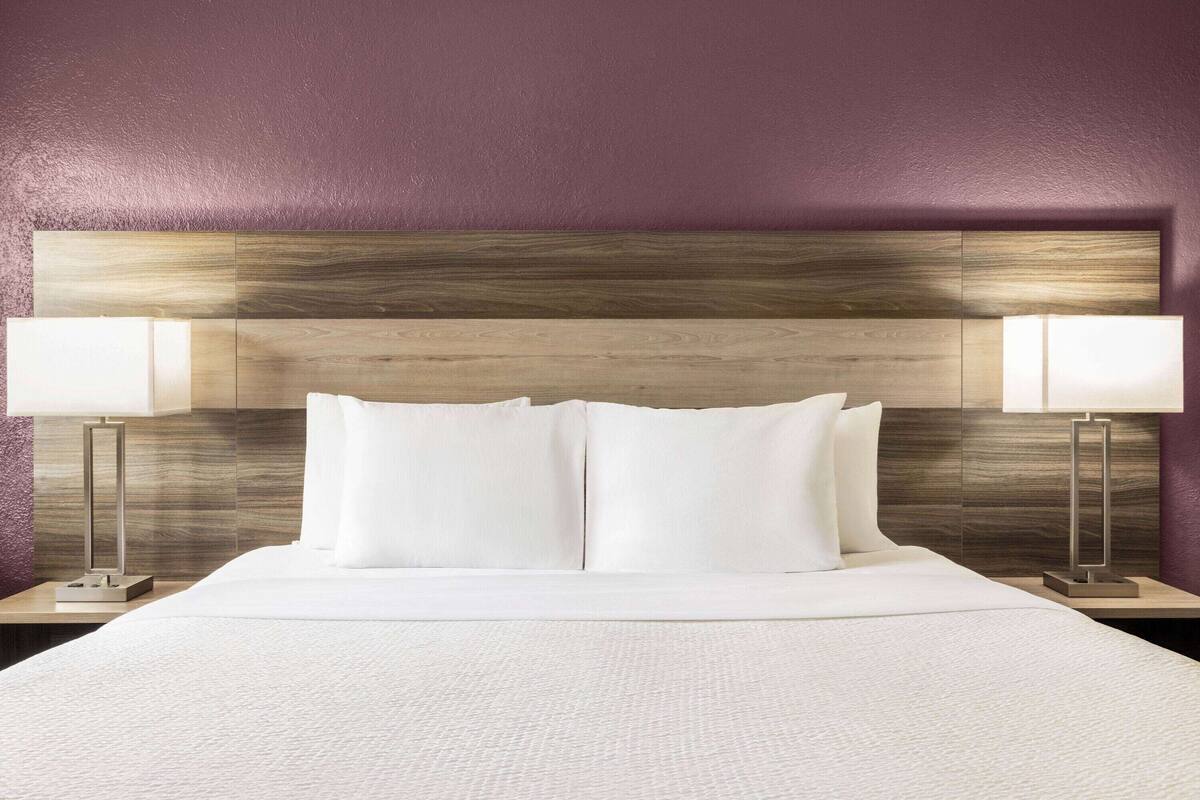 A neatly made bed with white linens and two bedside lamps on either side.