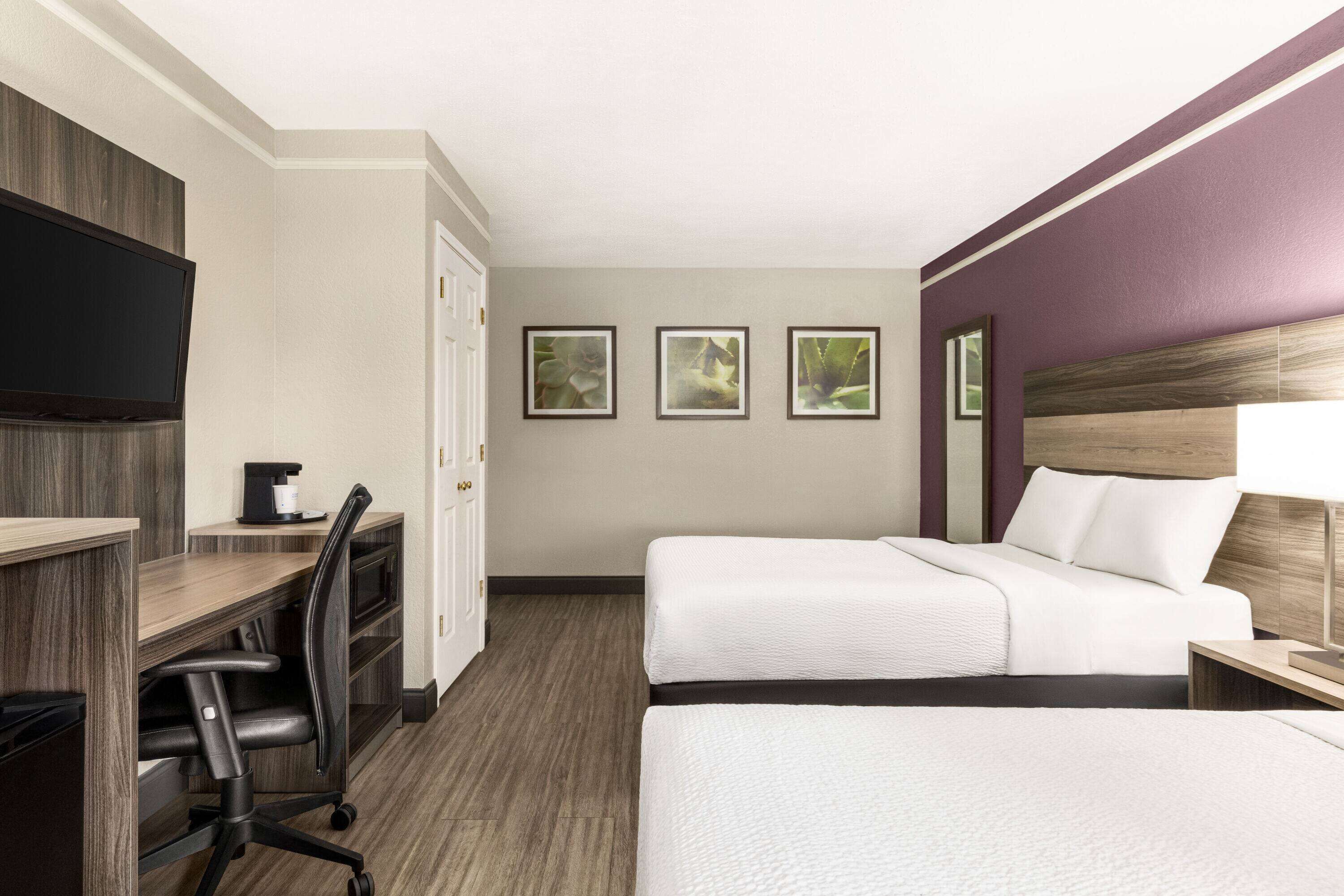 A hotel room with two beds, a desk, a chair, a TV, and framed pictures on the wall.