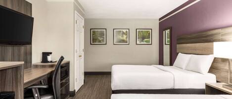 A hotel room with two beds, a desk, a chair, a TV, and framed pictures on the wall.