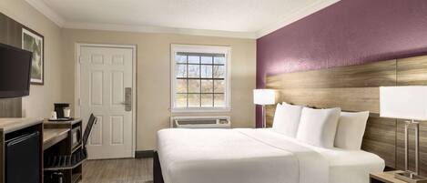A hotel room with a bed, desk, chair, TV, window, and lamp.