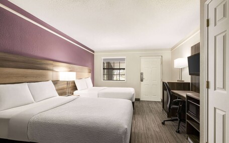 A hotel room with two beds, a desk with a chair, a TV, and a window.