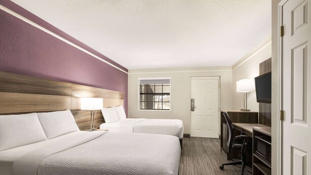 Une chambre d’hôtel avec deux lits, un bureau avec une chaise, une télévision et une fenêtre.