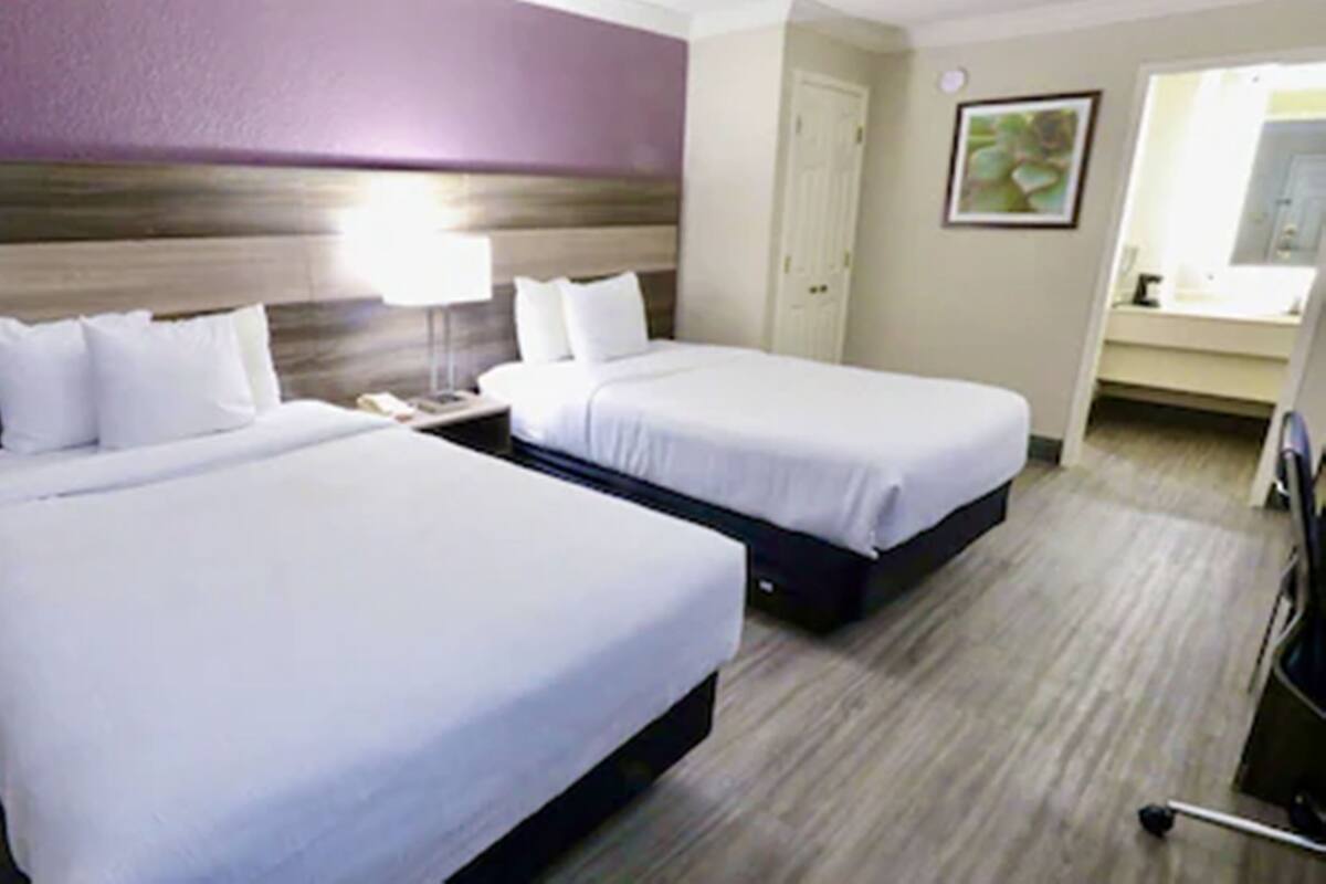 A hotel room with two beds, a bedside table, a lamp, and a chair.