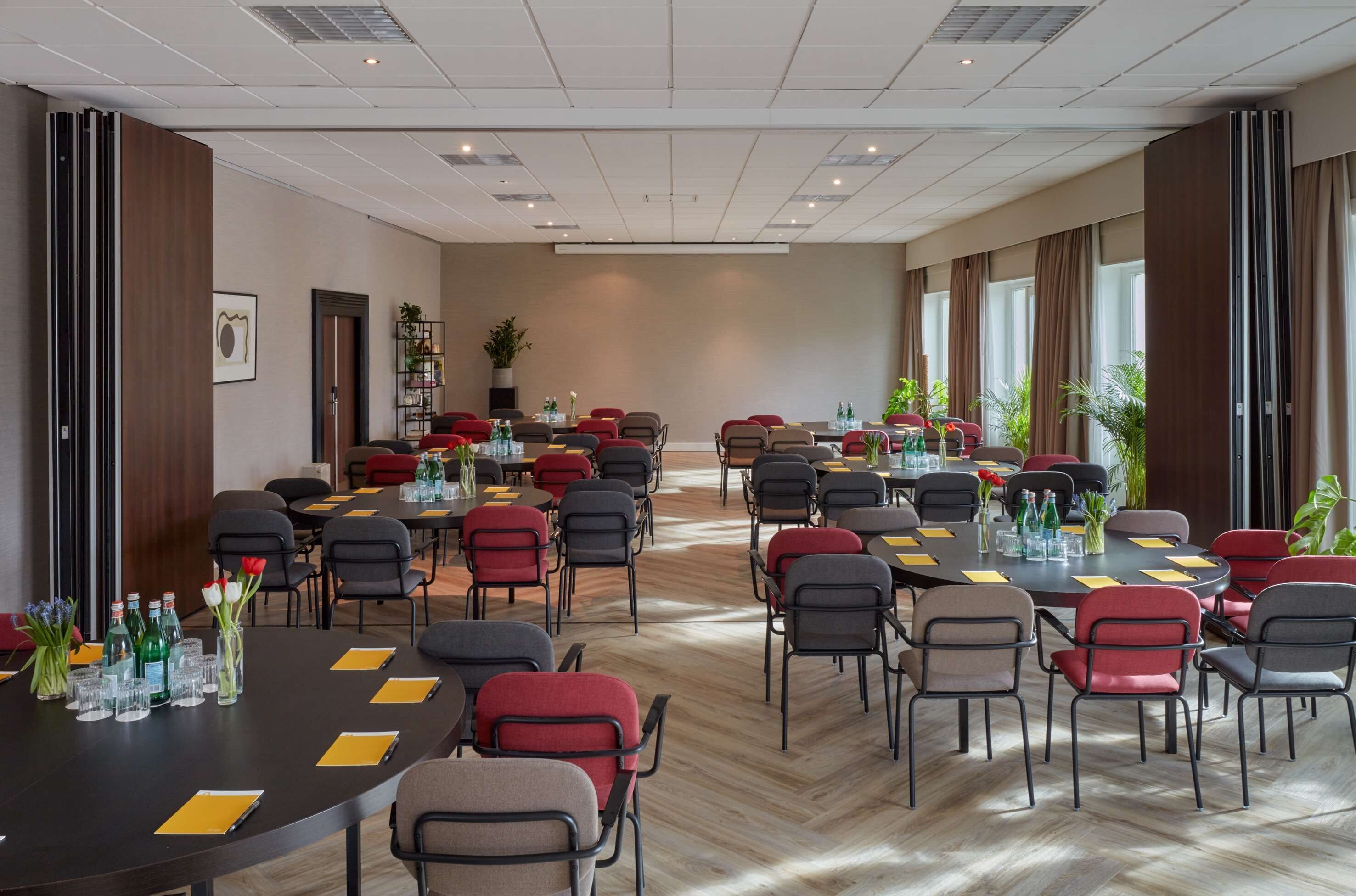 A conference room with multiple tables and chairs, equipped with water bottles, glasses, and notepads.