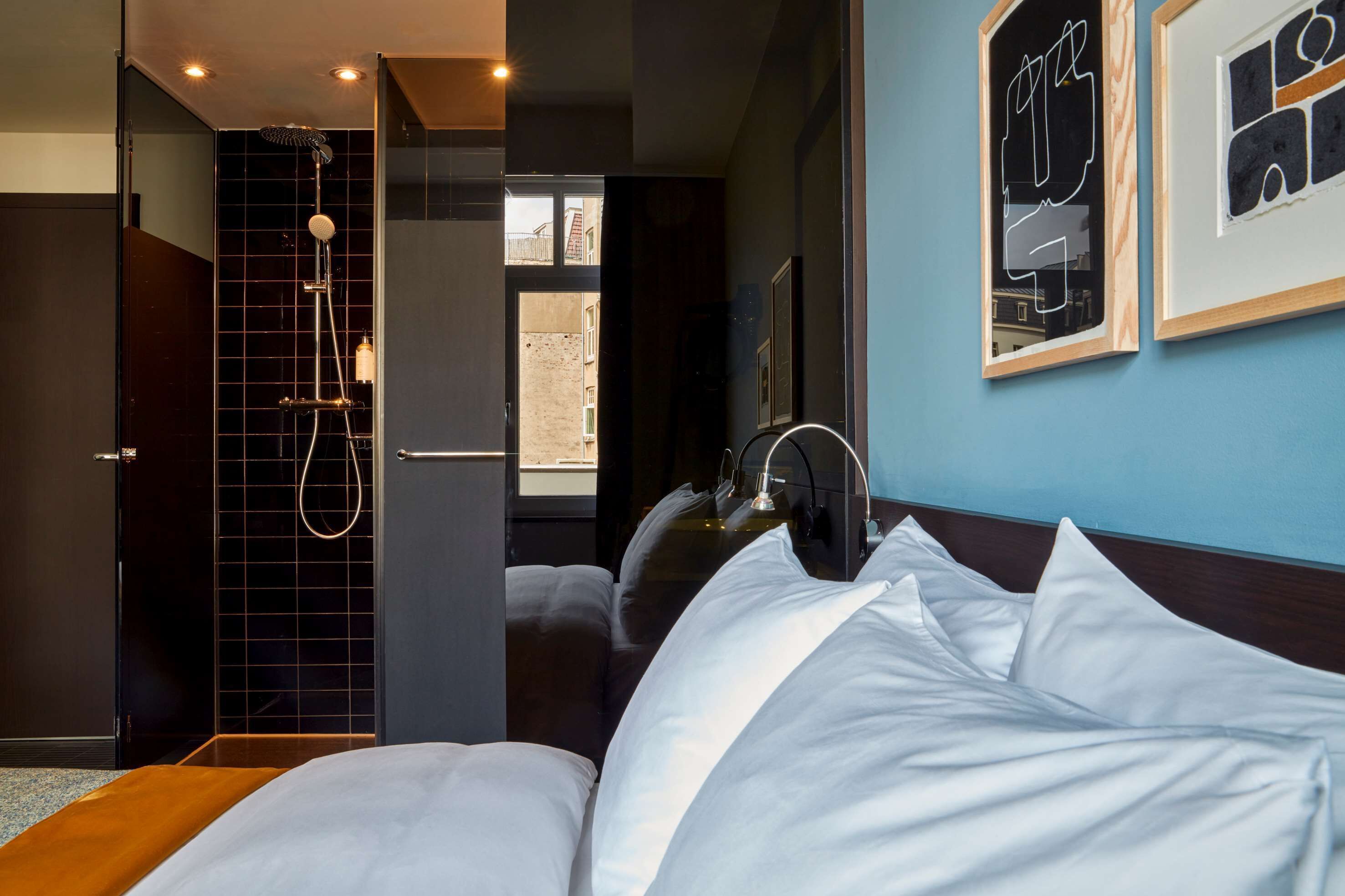 A hotel room with a bed, a shower, and two framed pictures on the wall.