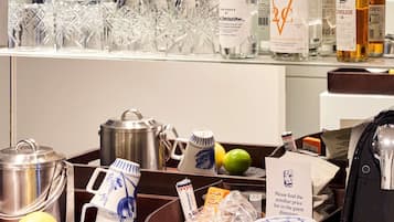A hotel minibar with various beverages, glasses, and a sign instructing to find the minibar price list in the guest room.