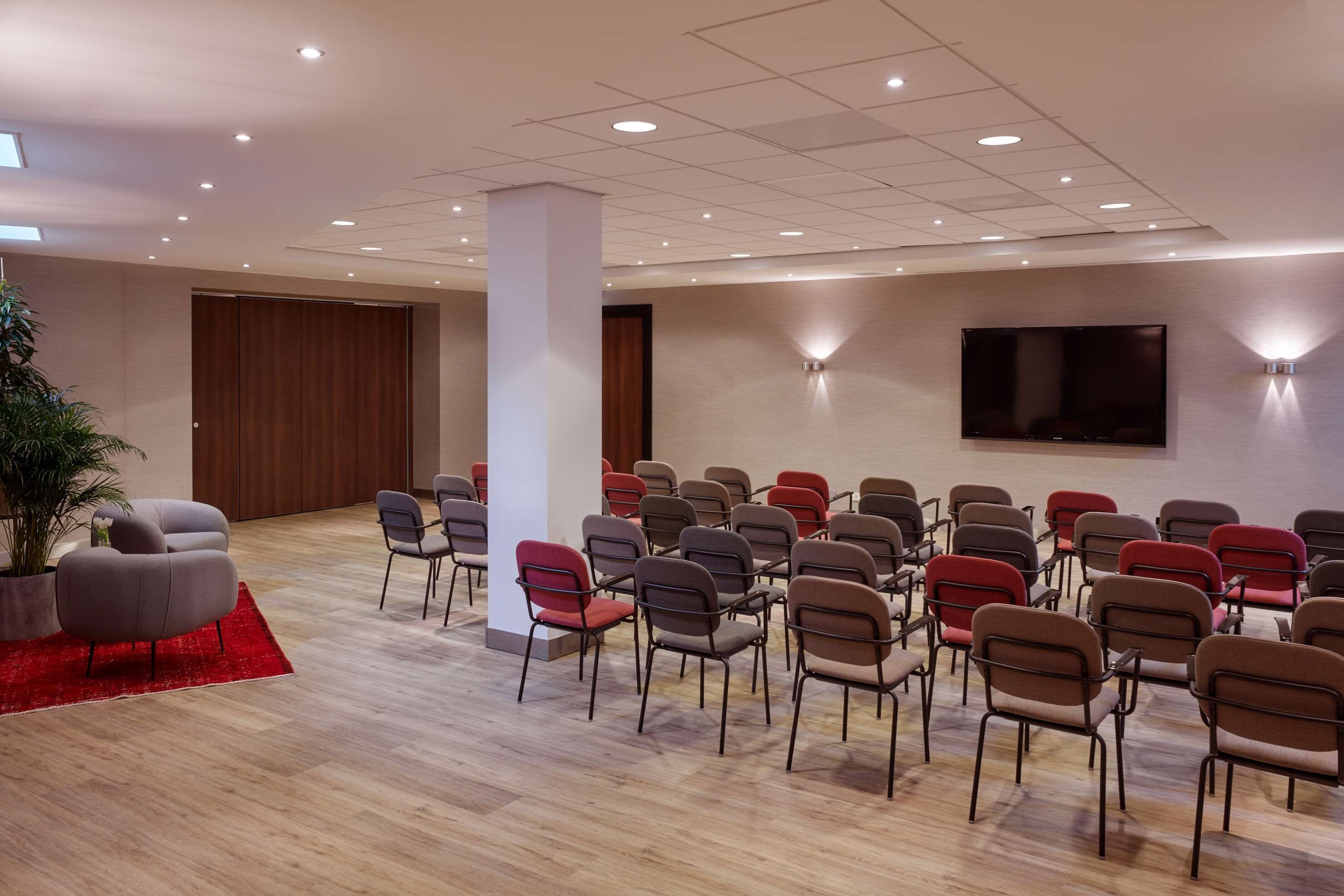 A conference room with rows of chairs, a large TV screen, and a potted plant.