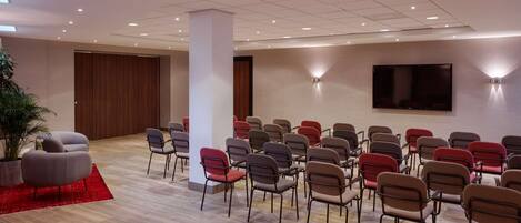 A conference room with rows of chairs, a large TV screen, and a potted plant.