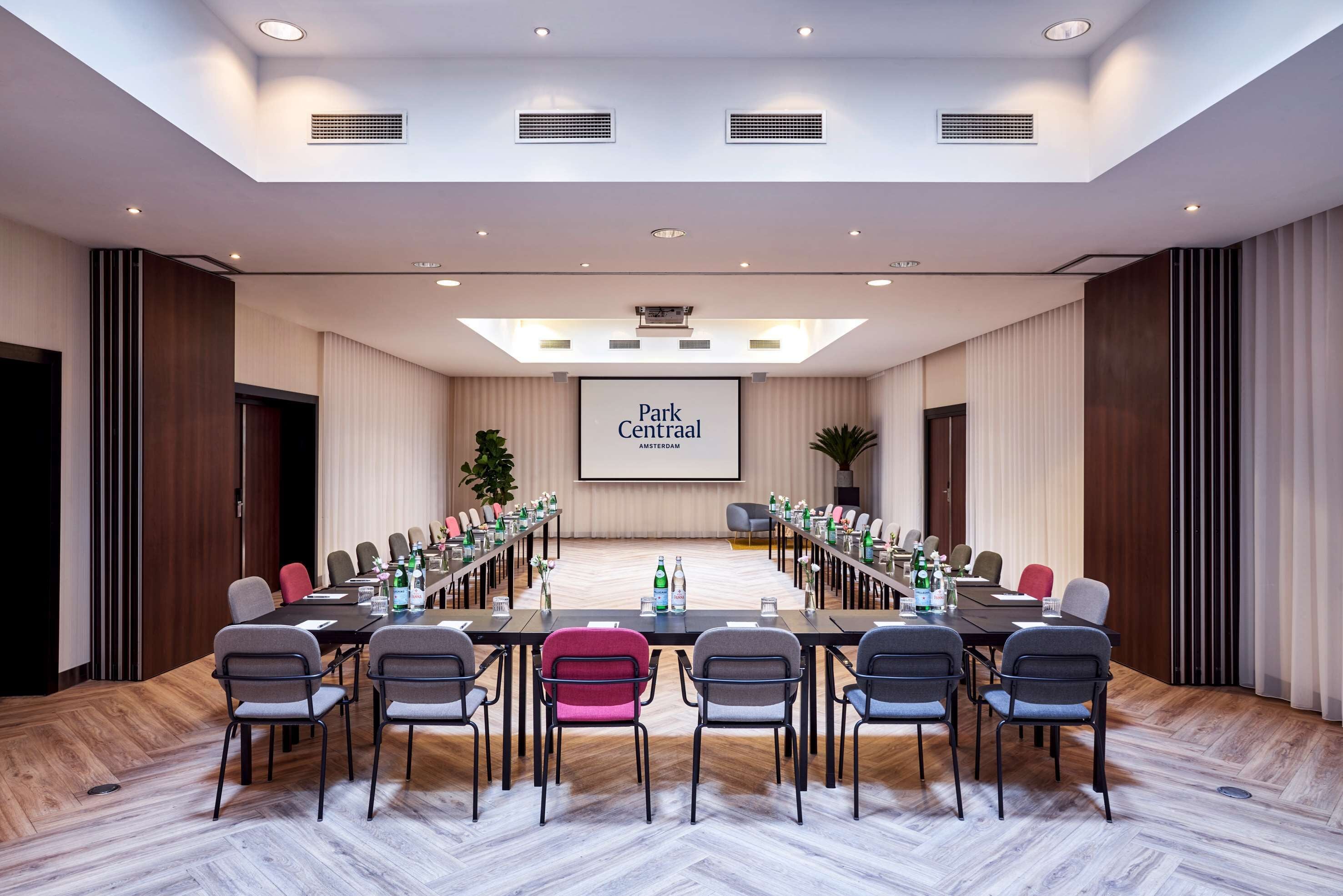 A conference room with a long table, chairs, a projector screen, and a large screen displaying "Park Centraal Amsterdam".