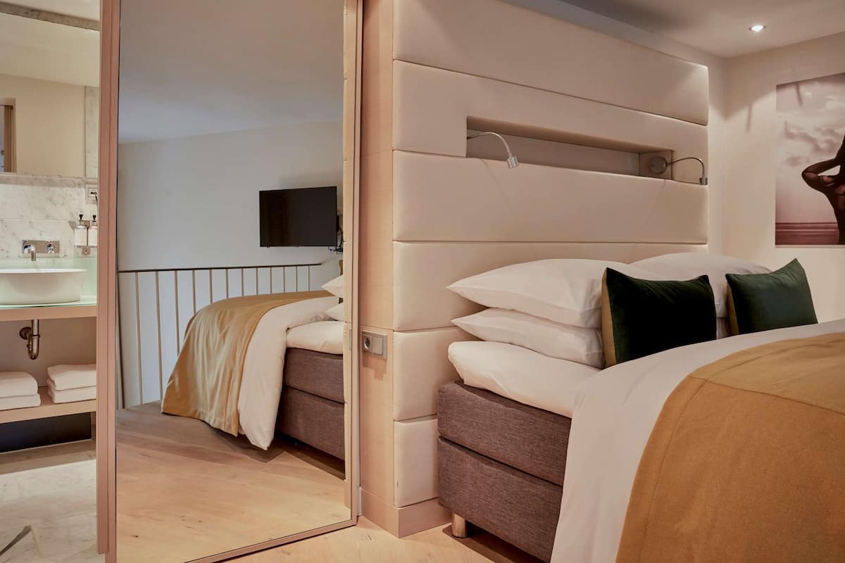 A modern hotel room with a large bed, a built-in TV, and a bathroom with a mirror and sink.