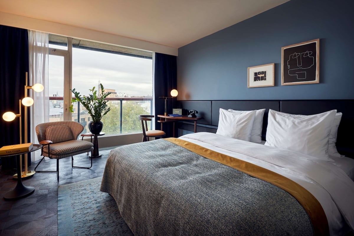A hotel room with a large bed, a desk, a chair, and a view of the city through the window.