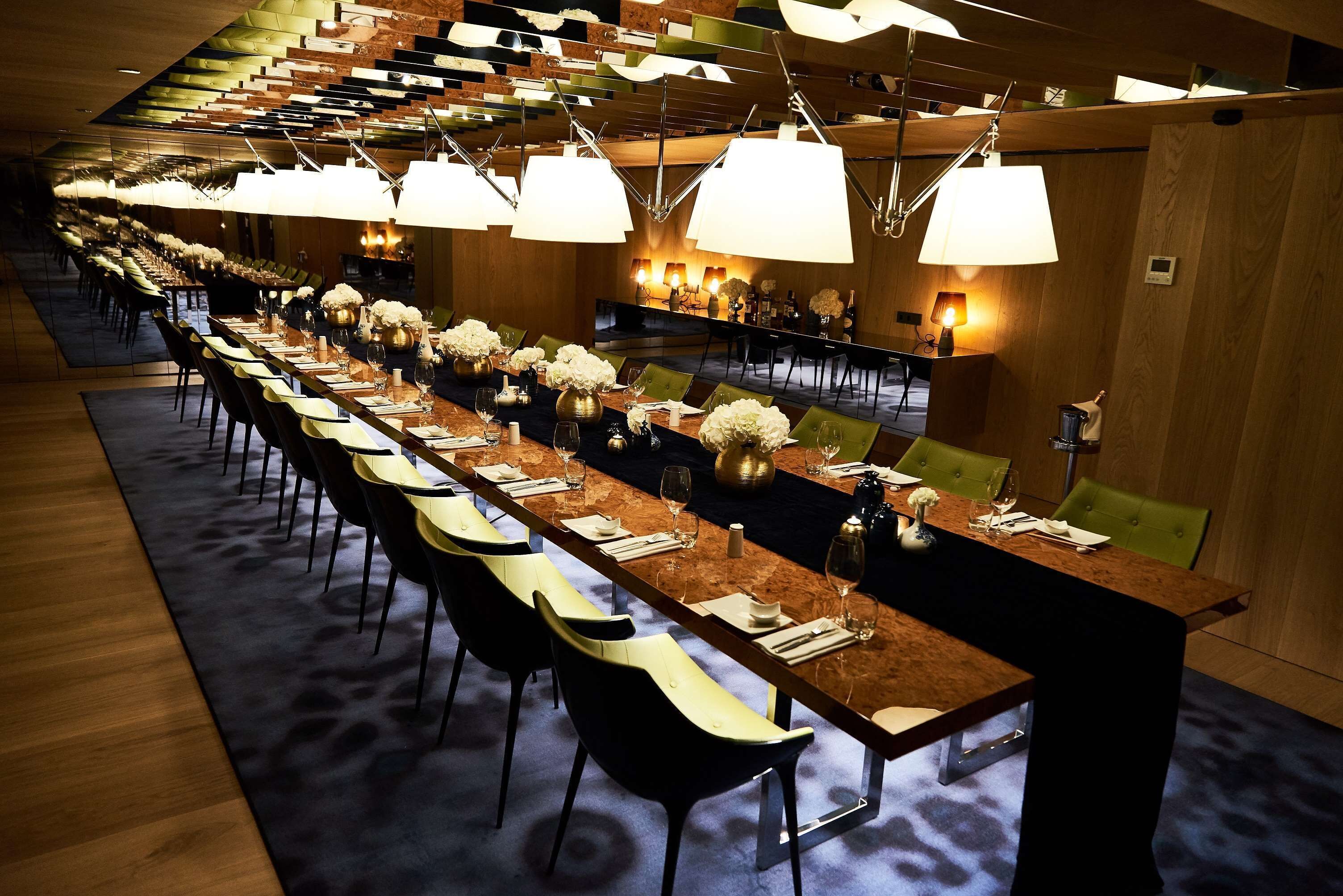 A long dining table with chairs, overhead lighting, and a carpeted floor.