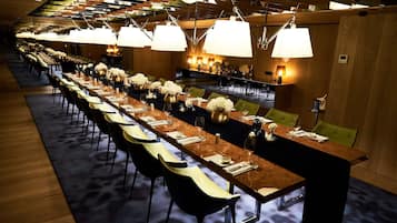 A long dining table with chairs, overhead lighting, and a carpeted floor.