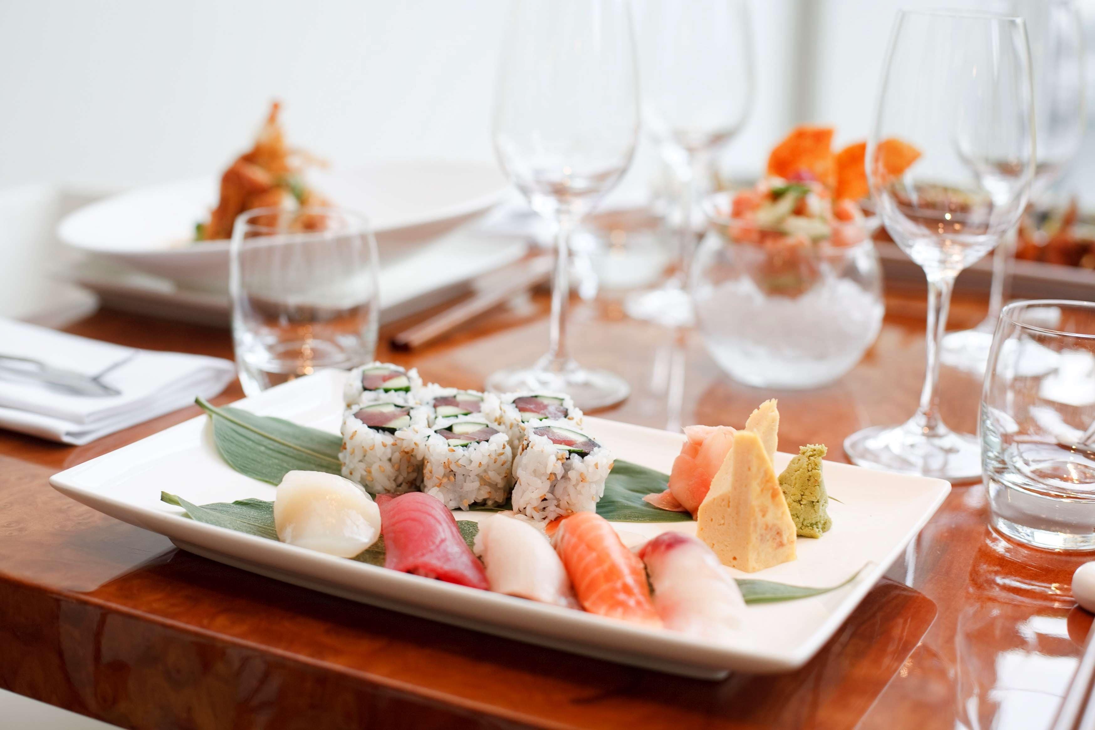 Een bord sushi met verschillende soorten sushi en sashimi, vergezeld van een glas water en een wijnglas.