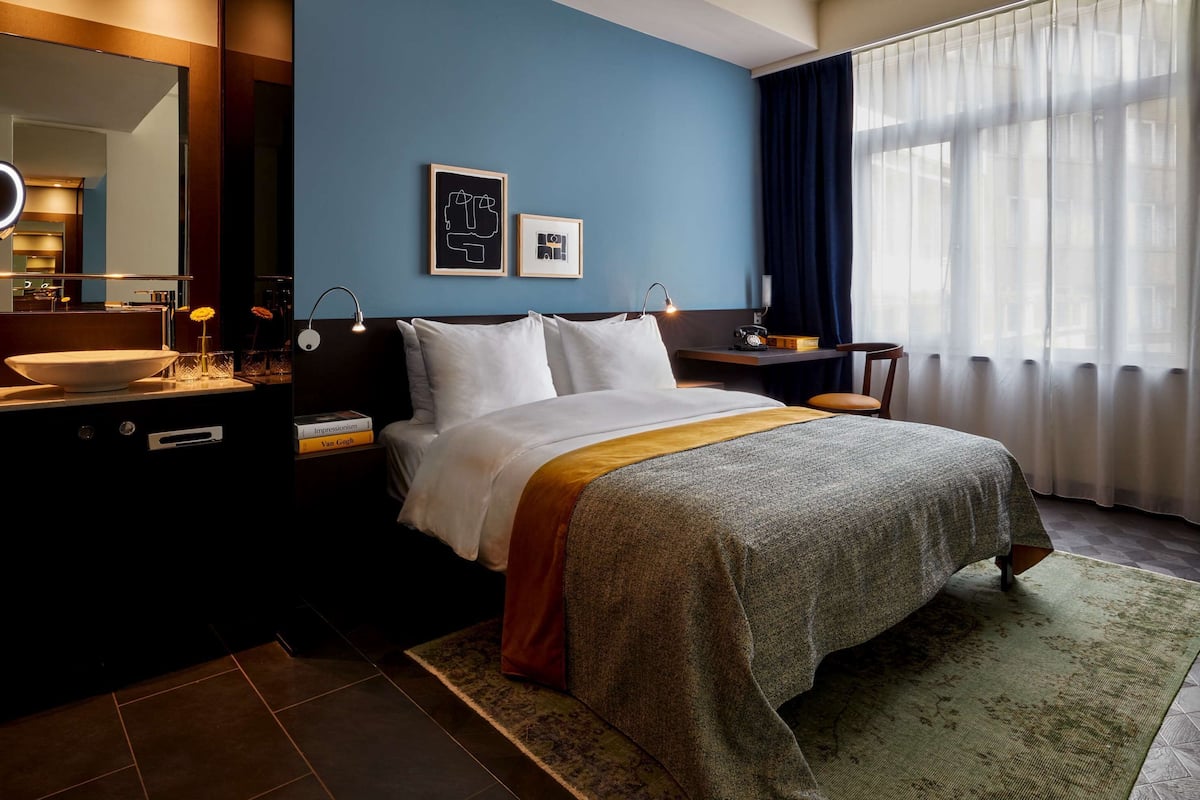 A hotel room with a bed, bedside table, mirror, and a window with curtains.