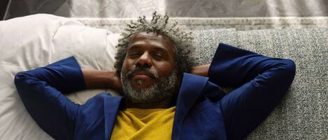 A person lying on a textured grey sofa with a white pillow, wearing a blue jacket and yellow shirt.