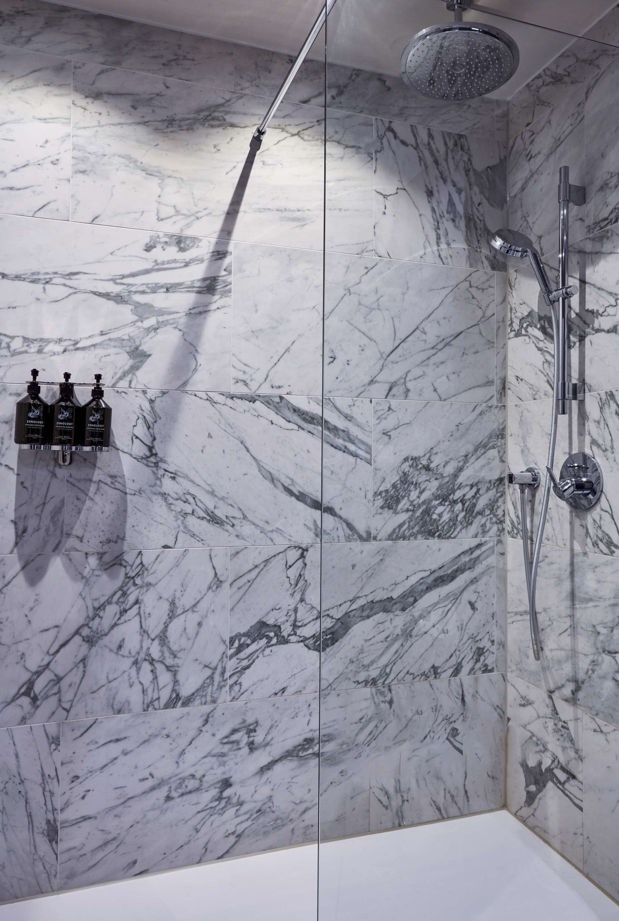 Une salle de bain moderne avec des murs en marbre, une douche en verre et un pommeau de douche à main.
