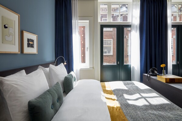 A hotel room with a bed, pillows, a framed artwork, a window with curtains, and a view of buildings outside. - Park Centraal Amsterdam, part of Sircle Collection (Amsterdam)