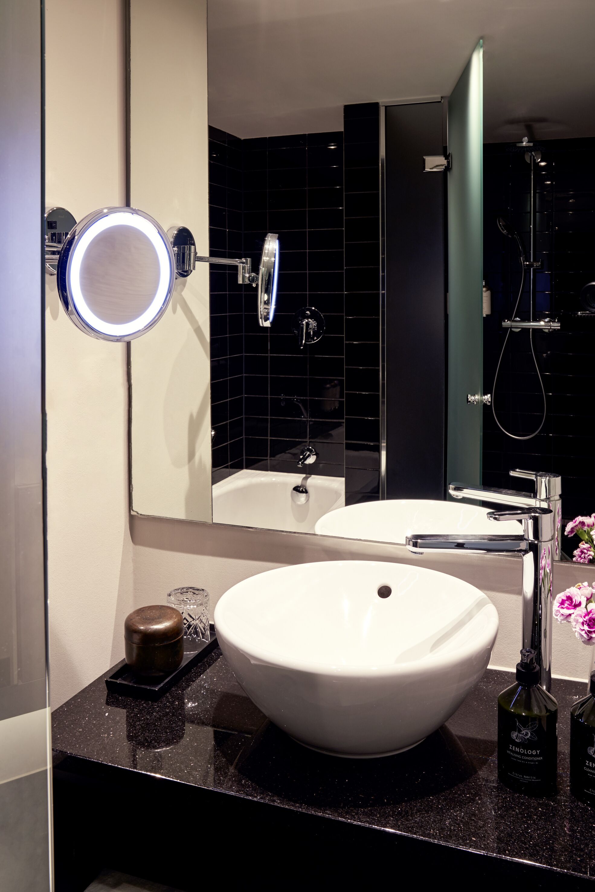 Une salle de bain moderne avec un lavabo blanc, un miroir rond avec un éclairage intégré et une douchette à main.