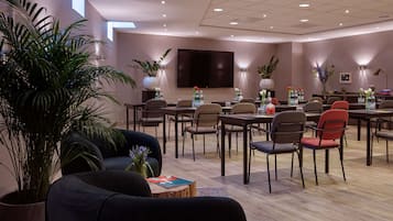 A modern conference room with a large flat-screen TV, multiple tables with chairs, and potted plants.