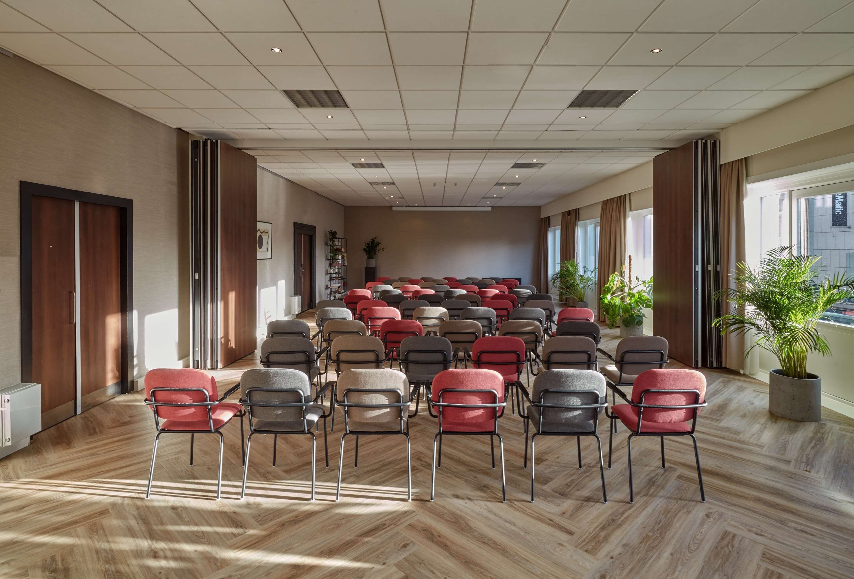 A conference room with rows of chairs, a wooden floor, and large windows.