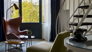 Ein modernes Wohnzimmer mit großem Fenster, einer Treppe und einer Sammlung gerahmter Kunstwerke an der Wand.