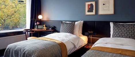 A hotel room with two beds, a nightstand, a lamp, and framed artwork on the wall.