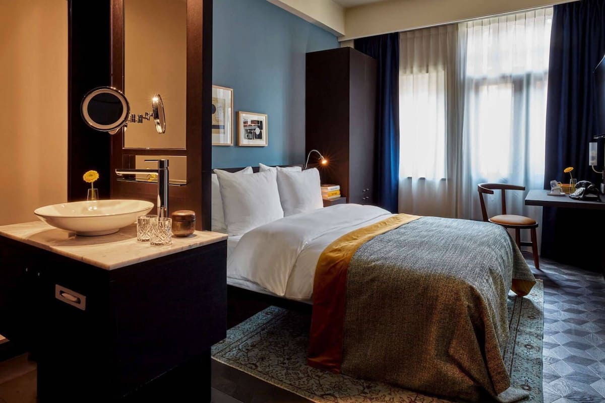 A hotel room with a bed, bedside table, mirror, and a desk with a chair.