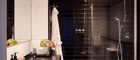 Un baño moderno con ducha de azulejos negros, lavamanos blanco y un espejo.