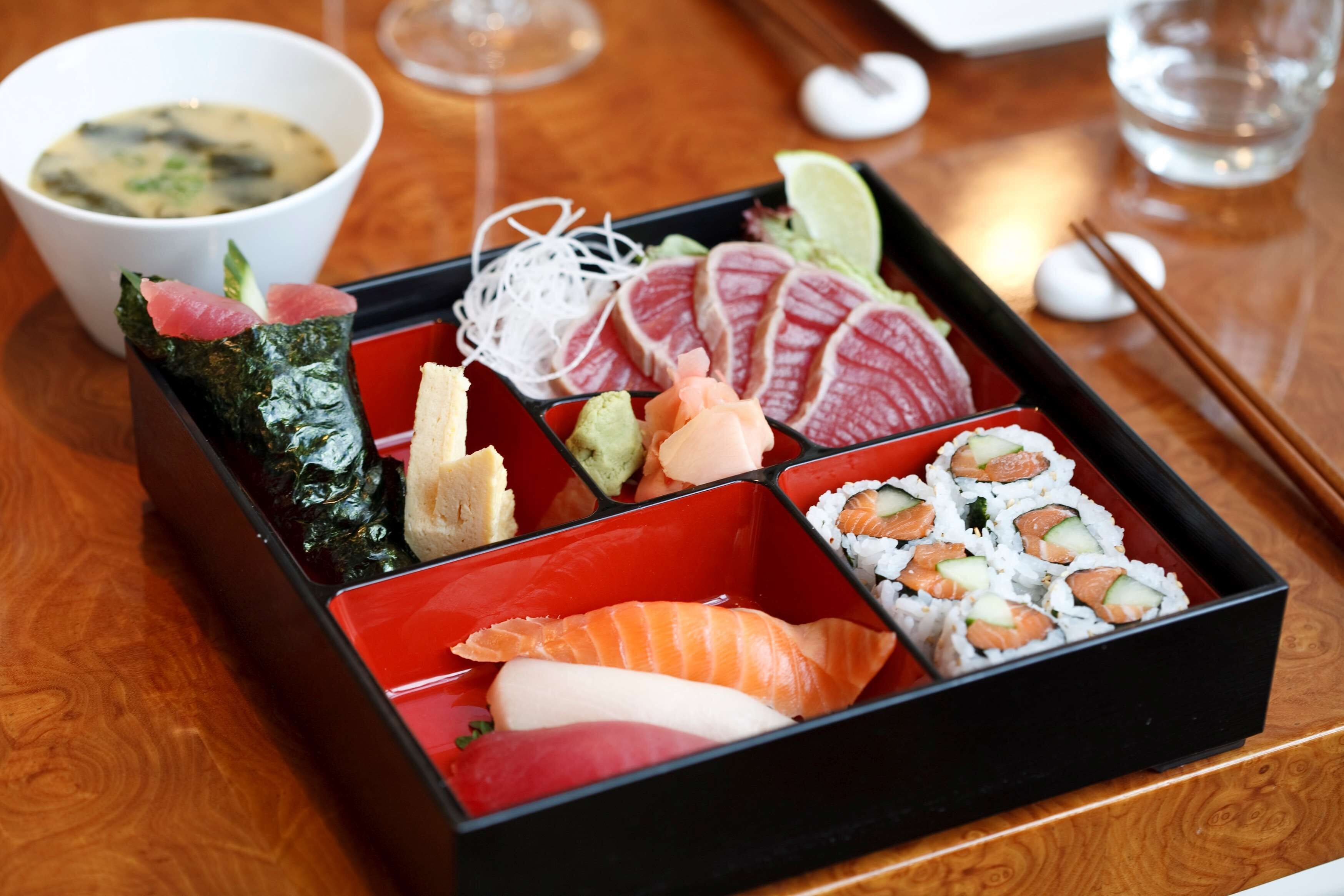 A bento box with various sushi and sashimi on a wooden table.