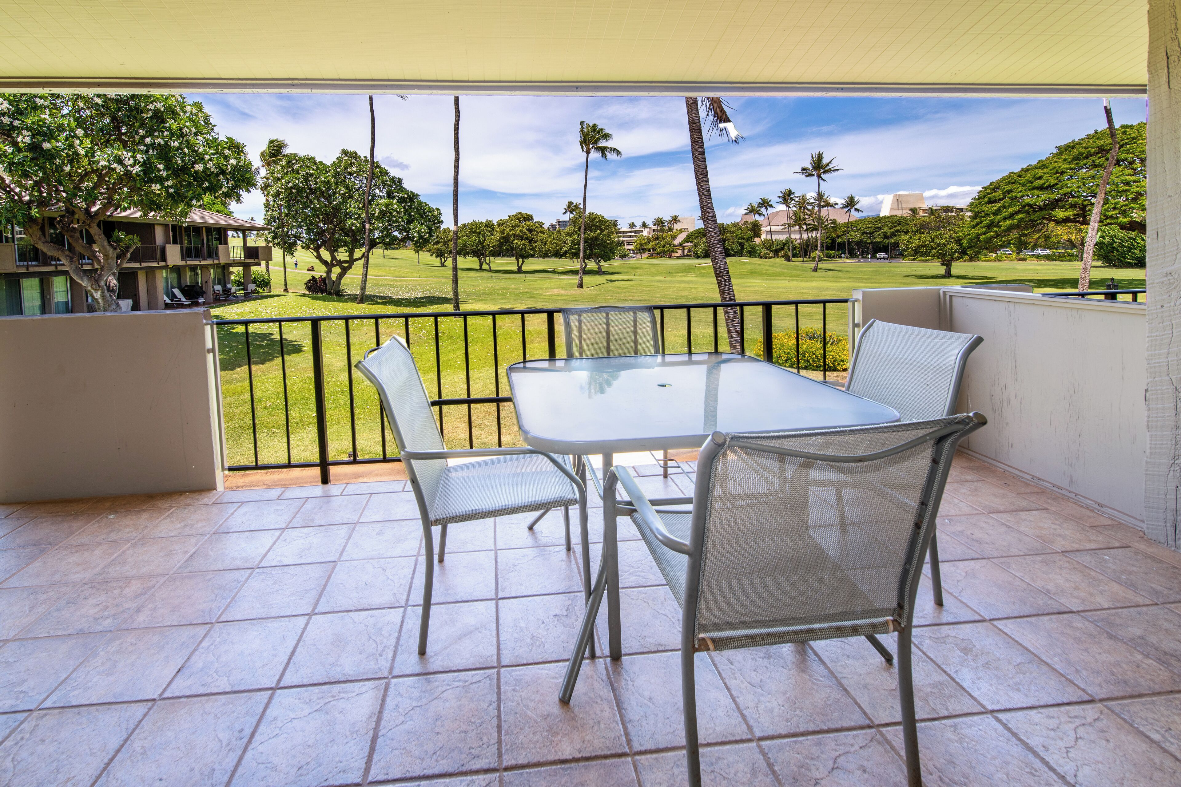 A covered patio with a table and chairs, offering a view of a golf course and palm trees.