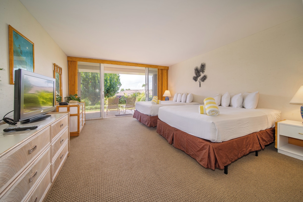 A hotel room with a television, two beds, a desk, and a view of the outdoors.