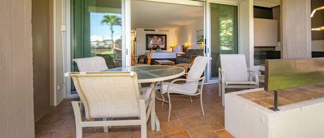 A dining area with a round table and four chairs, a small kitchen area with a stove and cabinets, and a sliding glass door leading to a balcony with a view of palm trees.
