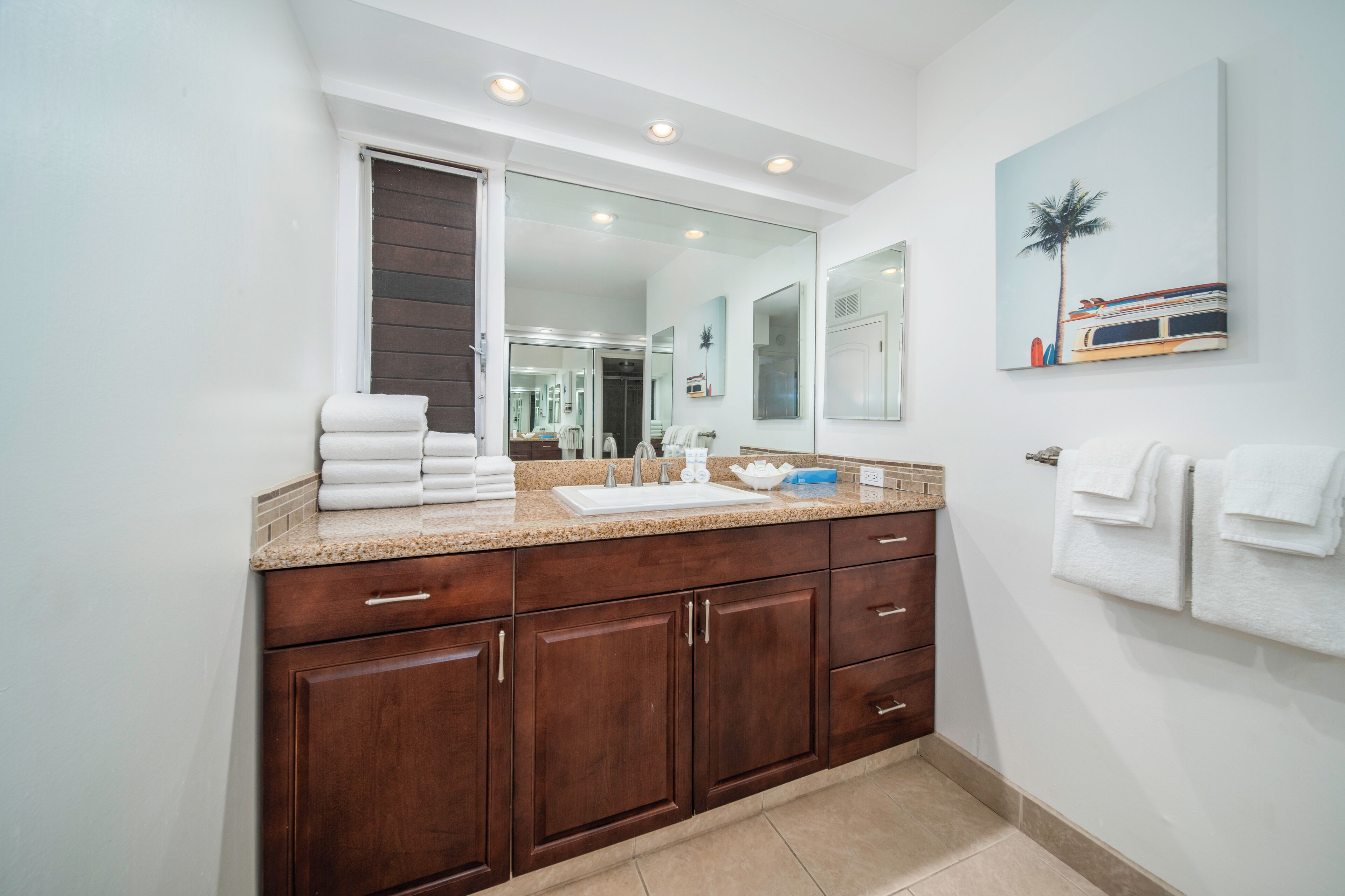 Un baño moderno con un espejo grande, armarios de madera oscura y encimera color beige.