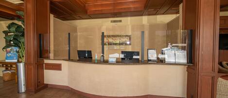 A reception area with a wooden reception desk, a large potted plant, and a ceiling fan.