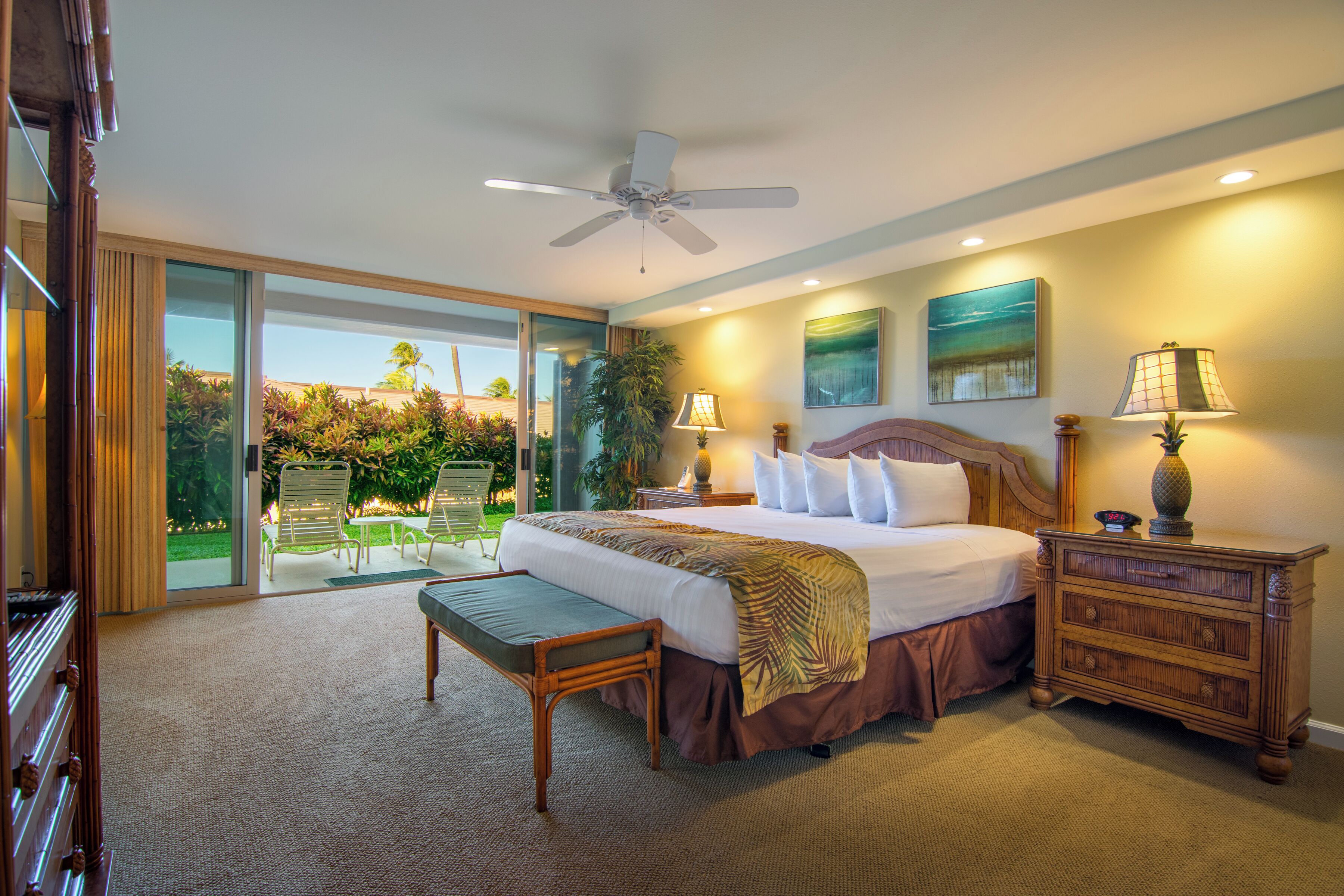 A spacious bedroom with a large bed, a ceiling fan, and a view of a garden through a sliding glass door.