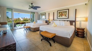 A hotel room with two beds, a desk, a chair, a bench, a ceiling fan, and a view of the outdoors.