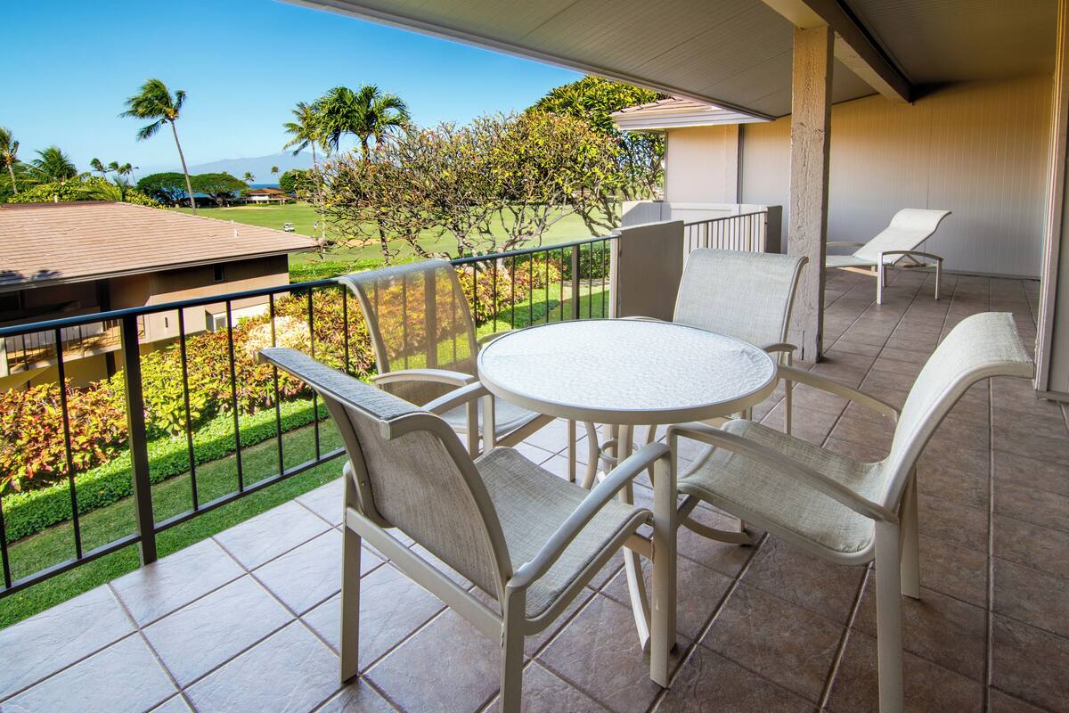 Uma varanda com uma mesa redonda e cadeiras, vista para um campo de golfe e uma palmeira.