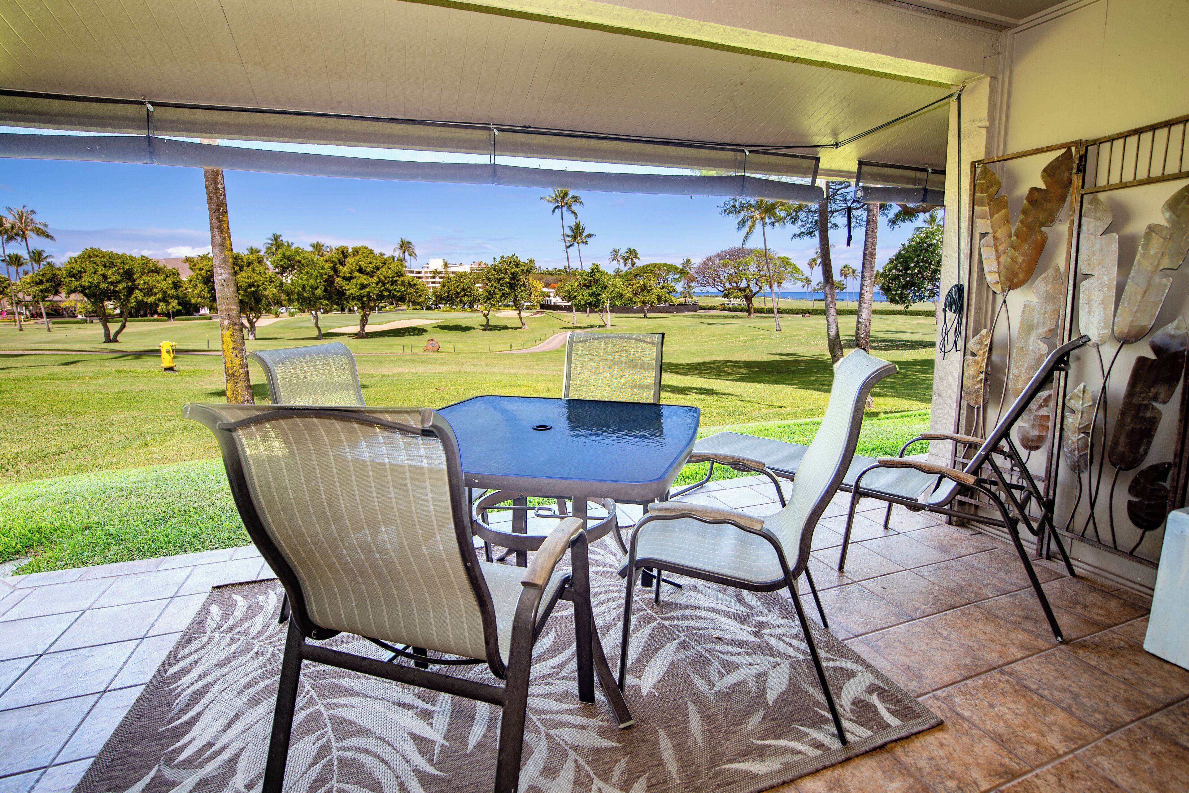 En overdækket terrasse med et bord og stole, udsigt til en golfbane og en dekorativ væg.