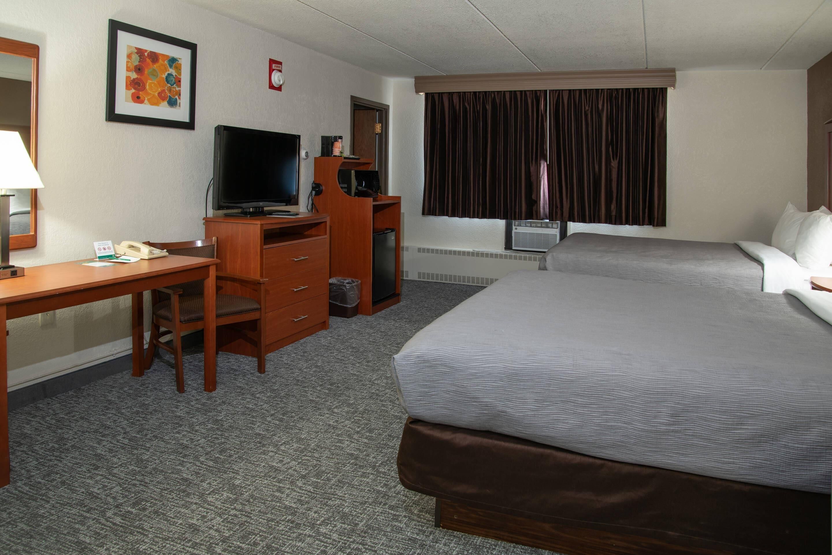 A hotel room with a bed, a desk with a television, a telephone, and a window with curtains.