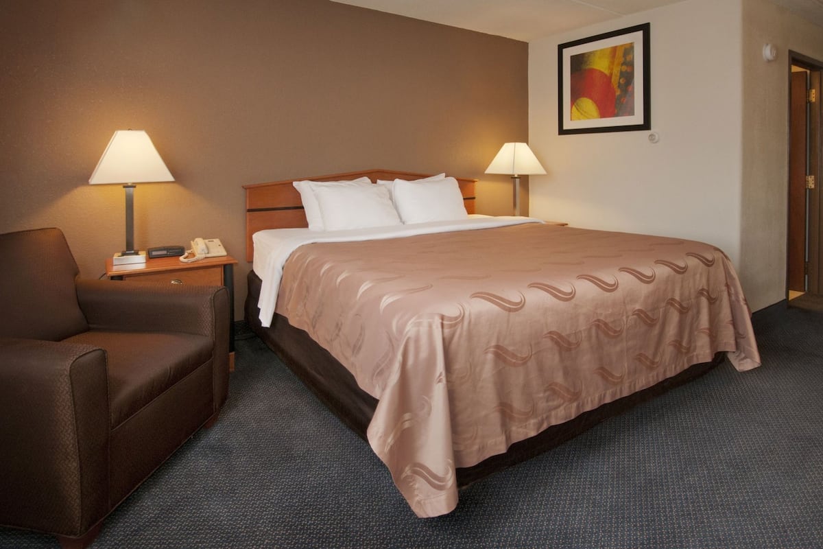 Una camera d'albergo con un letto, due lampade da comodino, una sedia, un tavolino e un quadro appeso al muro.
