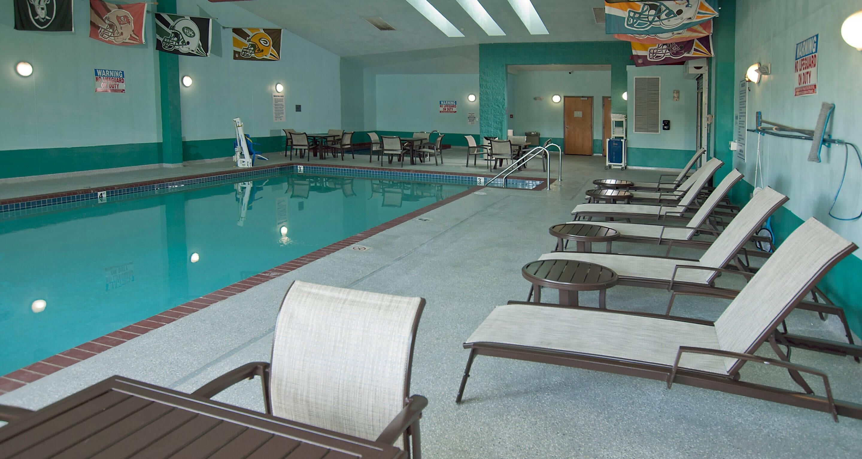 A swimming pool with lounge chairs and tables, a warning sign, and a door leading to another room.
