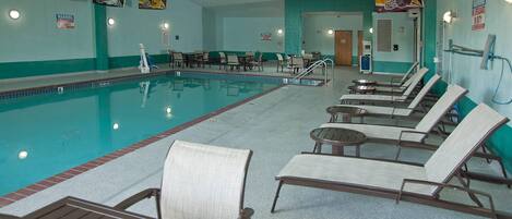 A swimming pool with lounge chairs and tables, a warning sign, and a door leading to another room.