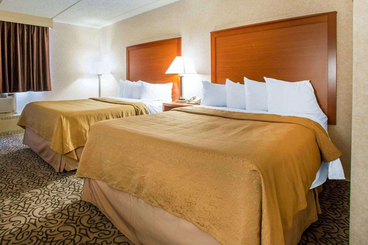 A hotel room with two beds, a wooden headboard, a bedside lamp, and a patterned carpet.