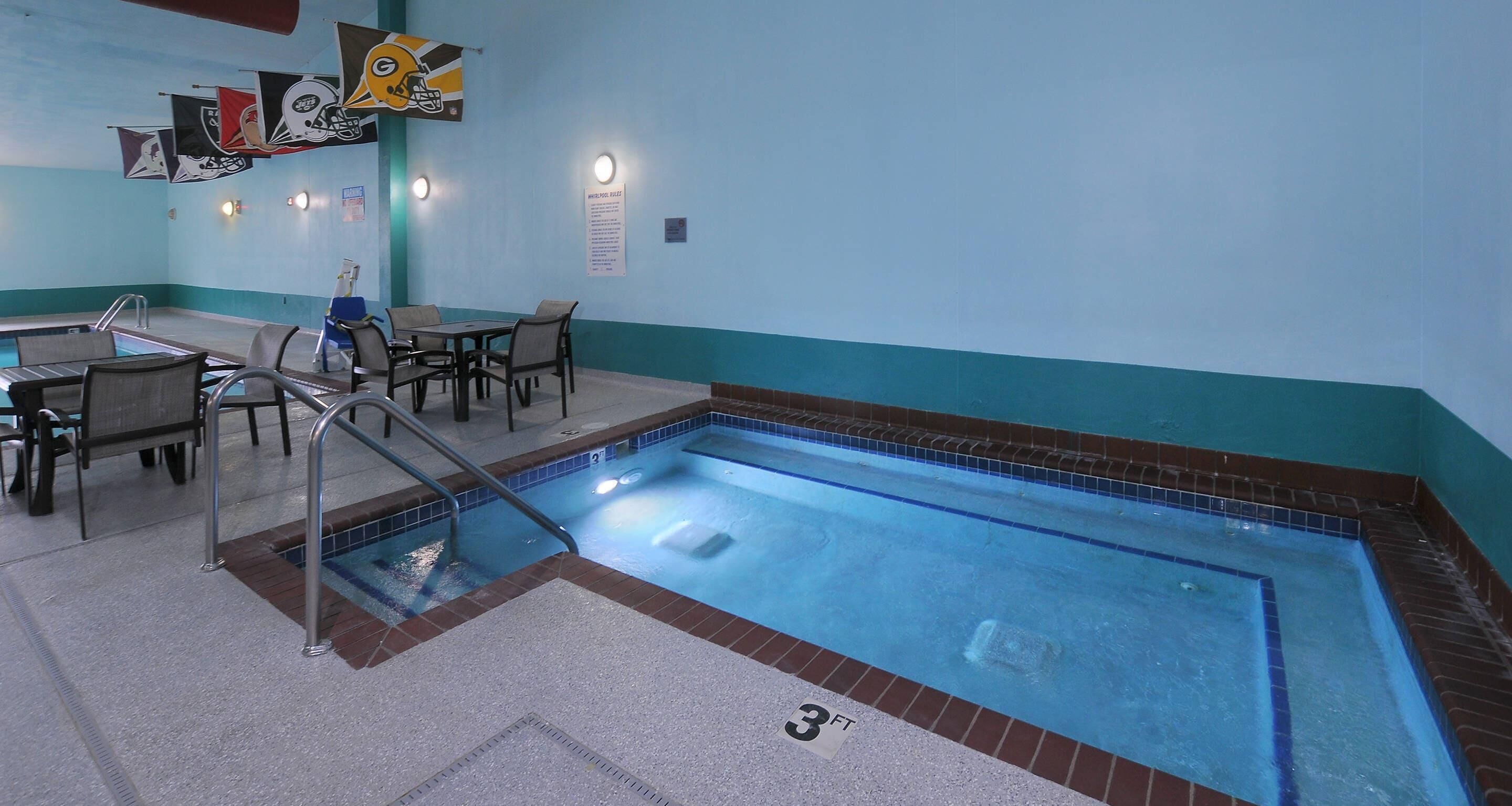 A swimming pool with a tiled edge, a seating area with chairs and tables, and flags on the wall.