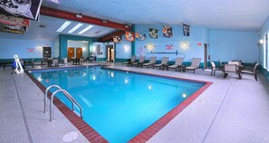 An indoor swimming pool with lounge chairs, a lifeguard stand, and wall decorations.