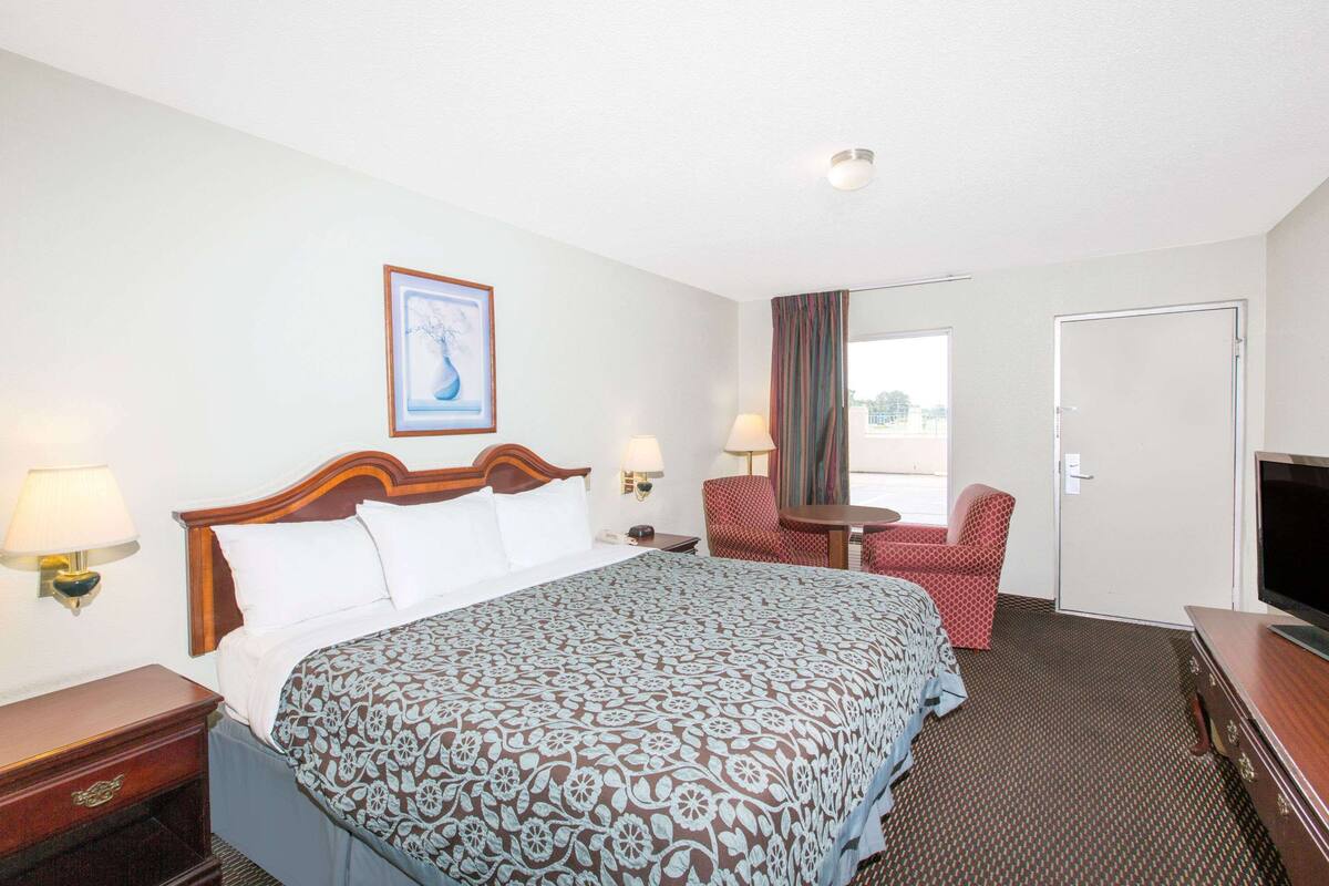 A hotel room with a large bed, two bedside tables with lamps, a TV, a chair, and a door.