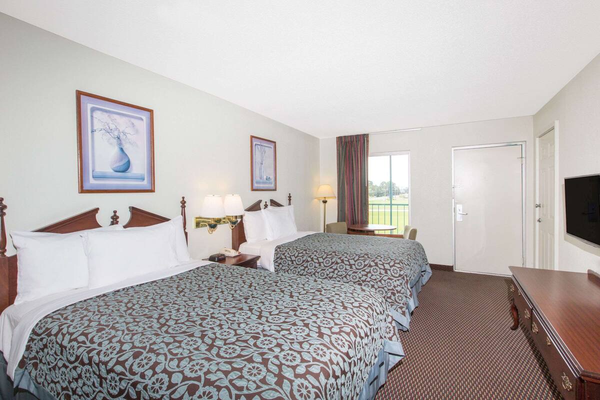 A hotel room with two beds, a television, a desk, and a window with curtains.