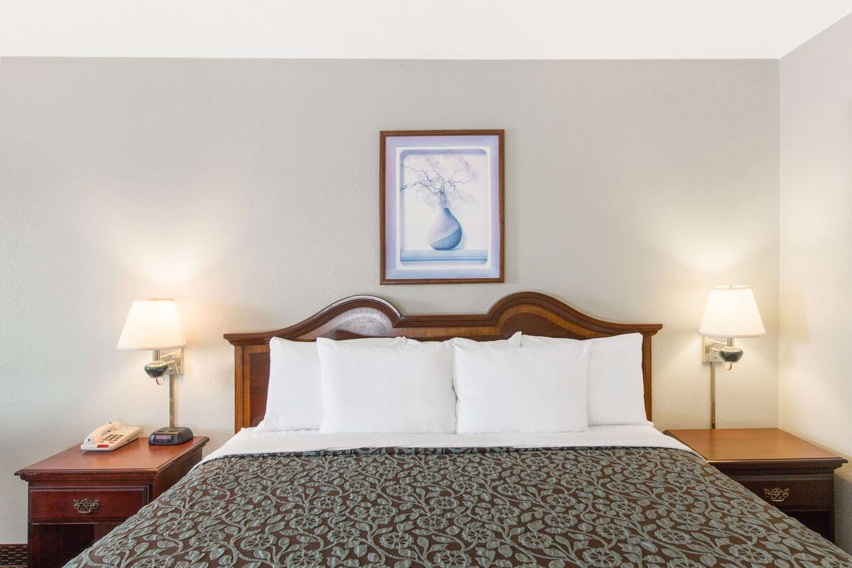 A hotel room with a bed, two bedside tables, a nightstand, a lamp, and a framed picture on the wall.