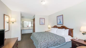 A hotel room with a bed, bedside tables, a TV, a mirror, and artwork on the walls.